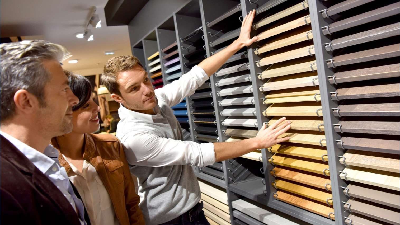 salesman in a kitchen retail store showcasing flooring options to a couple