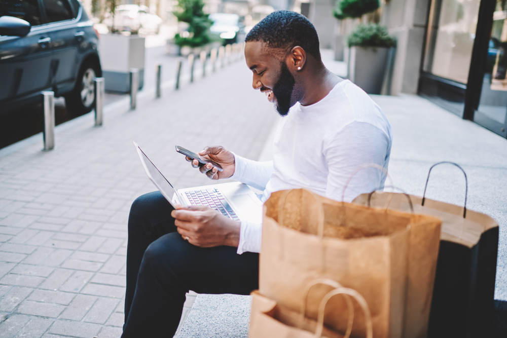 man designing on laptop while completing his purchase journey using his smartphone